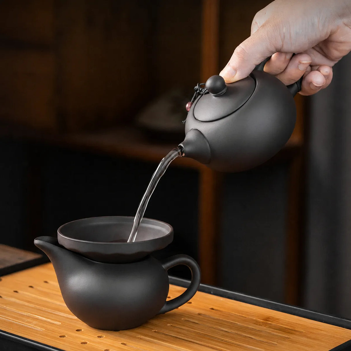Purple clay teapot pouring tea through a strainer on a bamboo tea tray
